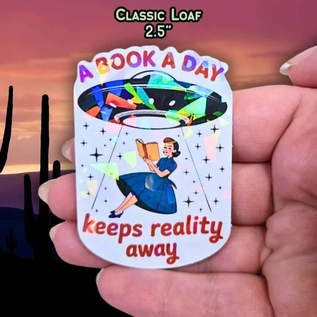A Book A Day Keeps Reality Away – Holographic Book Lover Sticker, Alien UFO Abduction Reading Sticker, Bookish Sticker, Sci - Fi Reader Gift - Holographic Sticker | The TabbyLoaf