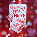 Star holographic We’re A Perfect Match sticker with red matchbox and burning heart match, cute pun design for couples, gifts, and Valentine’s decor